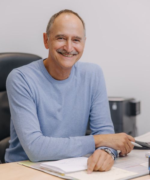 Hausarzt Dr. Hendrik Doßow aus Magdeburg lächelt freundlich an seinem Schreibtisch in der Praxis.