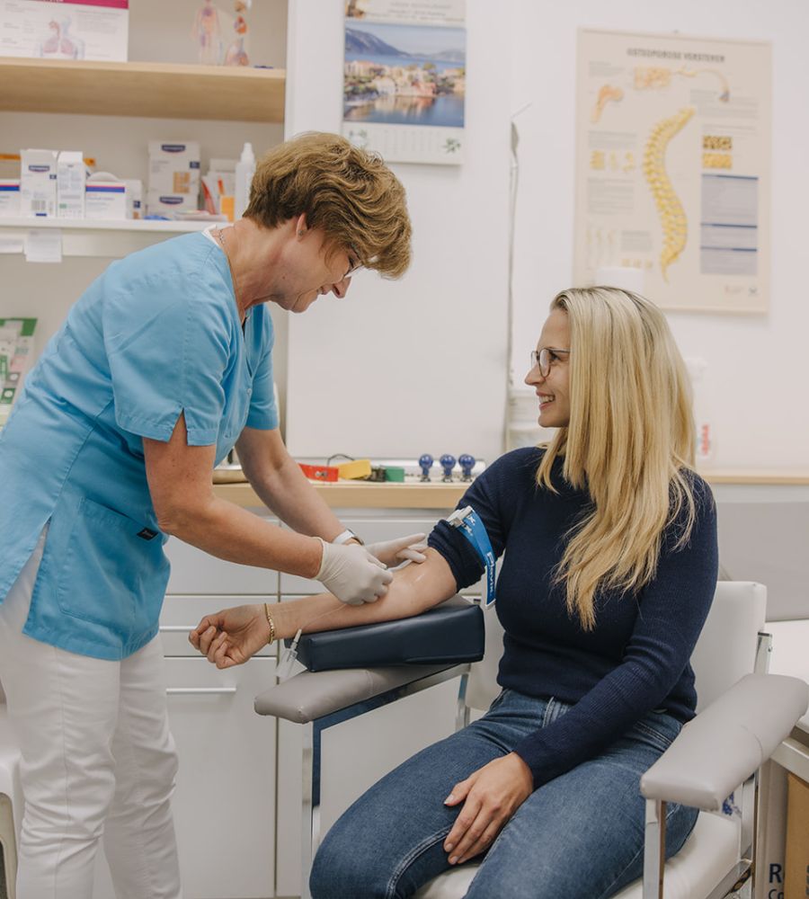 Medizinische Fachangestellte nimmt einer lächelnden Patientin Blut ab in der Hausarztpraxis Magdeburg.