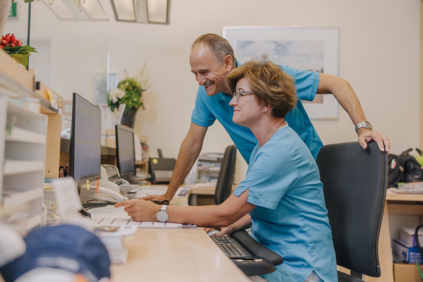 Hausarzt Dr. Doßow und Mitarbeiterin arbeiten gemeinsam am Empfangscomputer der Praxis in Magdeburg.