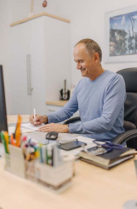 Hausarzt Dr. Doßow arbeitet konzentriert an Patientenunterlagen in seiner Praxis in Magdeburg.