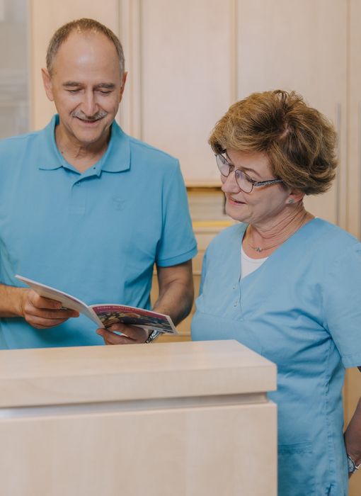 Hausarzt Dr. Doßow und Mitarbeiterin besprechen Unterlagen am Empfang der Praxis in Magdeburg.