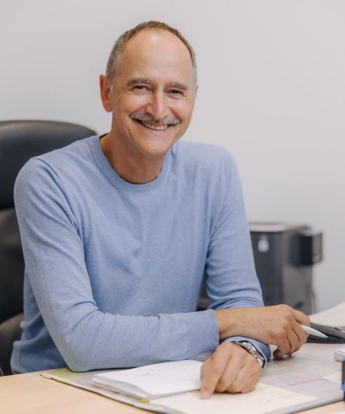 Hausarzt Dr. Hendrik Doßow aus Magdeburg lächelt freundlich an seinem Schreibtisch in der Praxis.